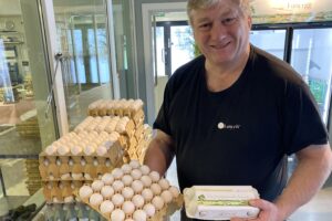 Erik fra Furu Egg smiler mens han viser frem dagsferske egg i gårdsbutikken